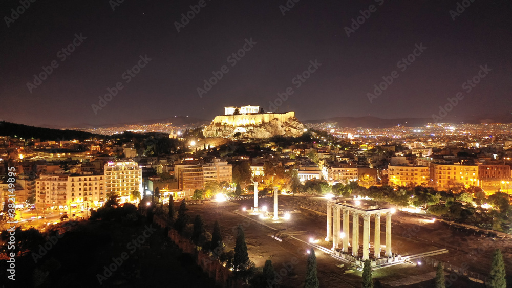 Aerial drone night shot of illuminated iconic Temple of Olympian Zeus and Acropolis hill and the Parthenon at the background, Athens, Attica, Greece