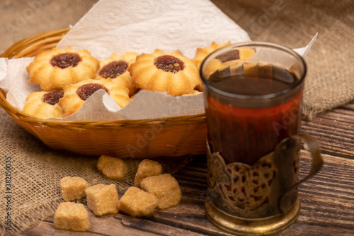 Homemade pastry cookies with jam and a faceted glass of tea in a vintage Cup holder on a background of homespun fabric with a rough texture, close-up, selective focus.
