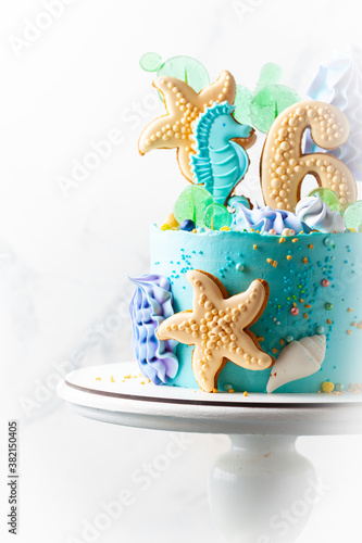 Blue and turquoise birthday cake with digit six. sea theme with seashells, sea horse and shingles gingerbread cookies. Nautical cake on the white background