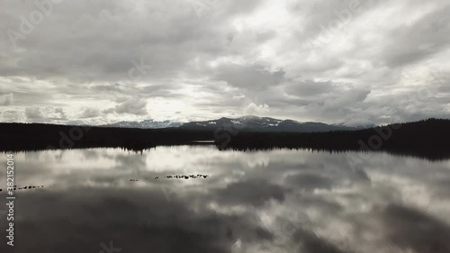 Epic mirror lake flying over with trees, mountain house, boat and mountains in the background reflecting in the perfectly still surface of water.  photo