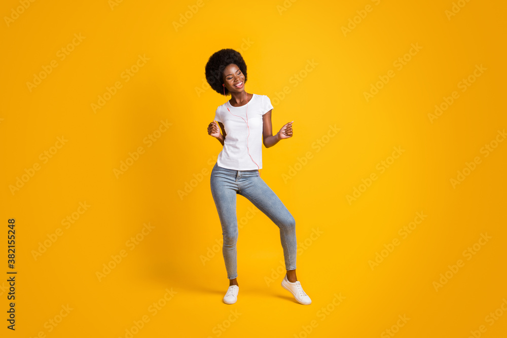 Full length body size photo of smiling girl with black skin listening music dancing keeping hands up isolated on bright yellow color background