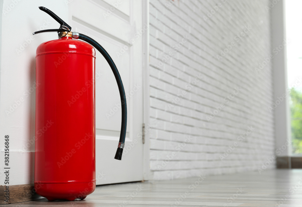 Fire extinguisher on floor near door indoors, space for text Fire extinguisher on floor near door indoors, space for text