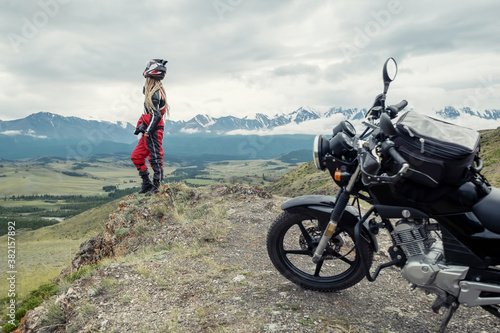 Fototapeta Naklejka Na Ścianę i Meble -  Female rider standing near her motorcycle  in mountains landscape. Long travel in Altai mountain in Russia