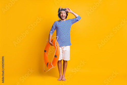 Ful size photo of excited guy hold life buoy touch scuba goggles wear blue striped shirt shorts isolated on yellow color background