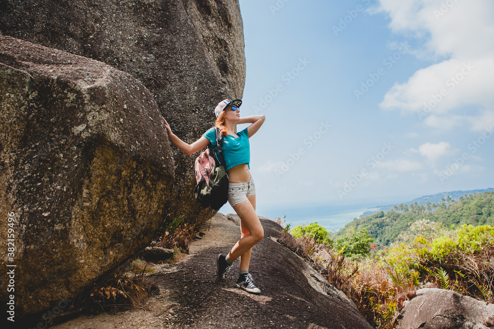 ginger woman traveling with backpack in mountains, tourist on summer vacation in thailand, posing in casual outfit wearing sunglasses