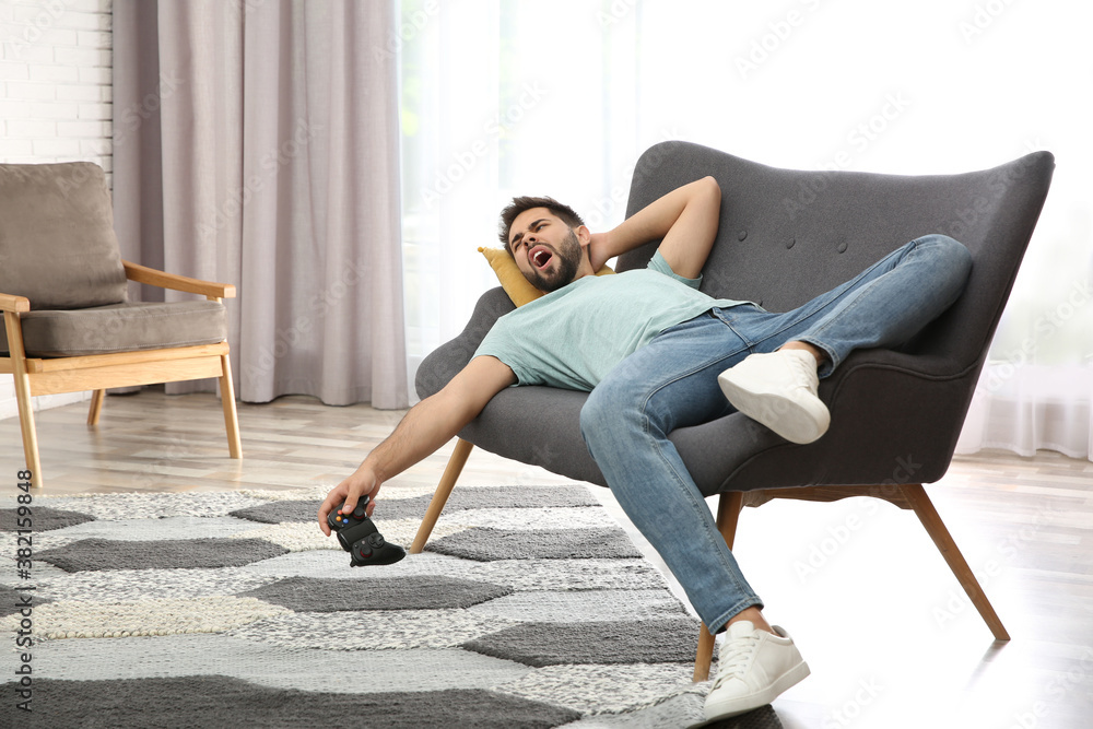 Lazy young man playing video game while lying on sofa at home