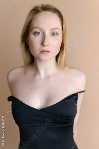 Graceful young woman in a black top posing against beige wall.