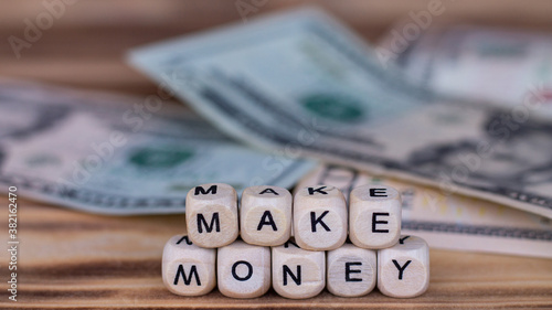 The words Make Money lined with letters on wooden cubes on the background of dollar bills.