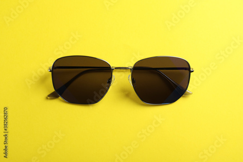 Stylish sunglasses on yellow background, top view