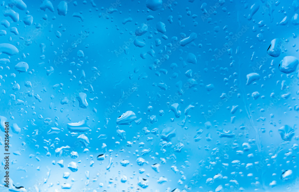 Water droplets from rain on the outside of a window with blue background. Close up. Water droplets from rain on the outside of a window with blue background. Close up.