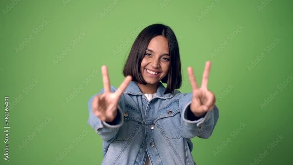 woman smiling and showing victory sign with a cheerful face on green screen chroma key background woman smiling and showing victory sign with a cheerful face on green screen chroma key background