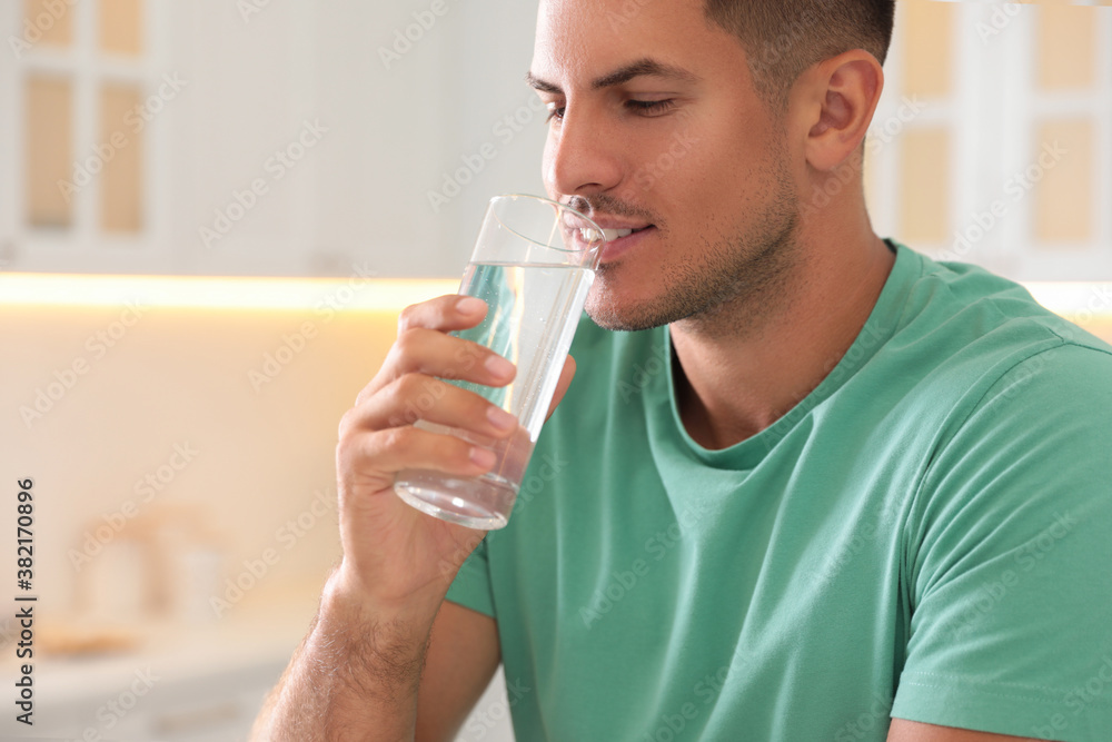Man drinking pure water from glass in kitchen, closeup Man drinking pure water from glass in kitchen, closeup