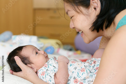 Asian mom hands around a young daughter lying in bed Smile and look at each other