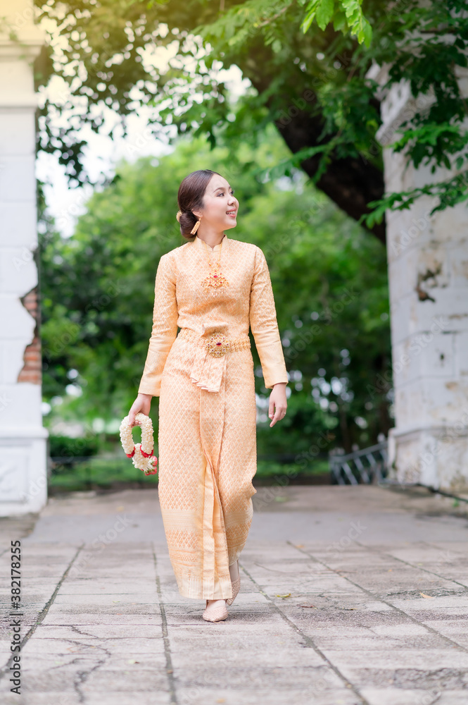 Elegant Thai woman in Thai dress adorned with precious jewelry walks holding flower garlands in Thai temple Elegant Thai woman in Thai dress adorned with precious jewelry walks holding flower garlands in Thai temple