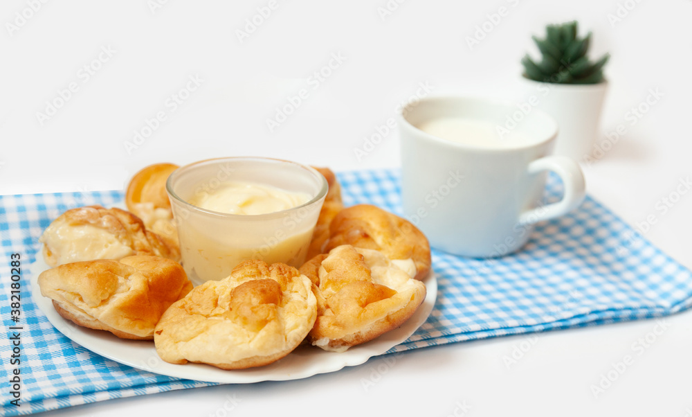 Small round eclairs or profiteroles lie on a blank background. Next to a plate with dessert on the table is a crumb of milk. Copy space Small round eclairs or profiteroles lie on a blank background. Next to a plate with dessert on the table is a crumb of milk. Copy space