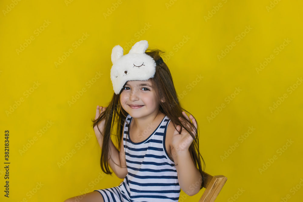A little girl on a bright yellow background wearing a fashion accessory sleep mask. A little girl on a bright yellow background wearing a fashion accessory sleep mask.