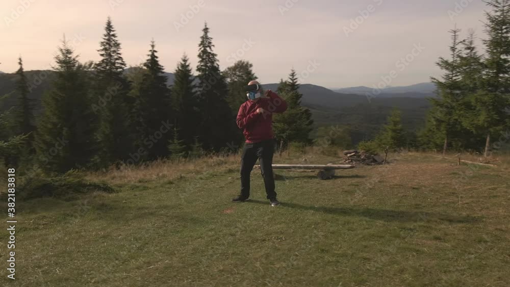 4K Conceptual aerial drone shot of young hairless man dancing alone during the coronavirus covid pandemia in VR glasses helmet virtual reality and protecting mask with filters in the wild mountains 4K Conceptual aerial drone shot of young hairless man dancing alone during the coronavirus covid pandemia in VR glasses helmet virtual reality and protecting mask with filters in the wild mountains