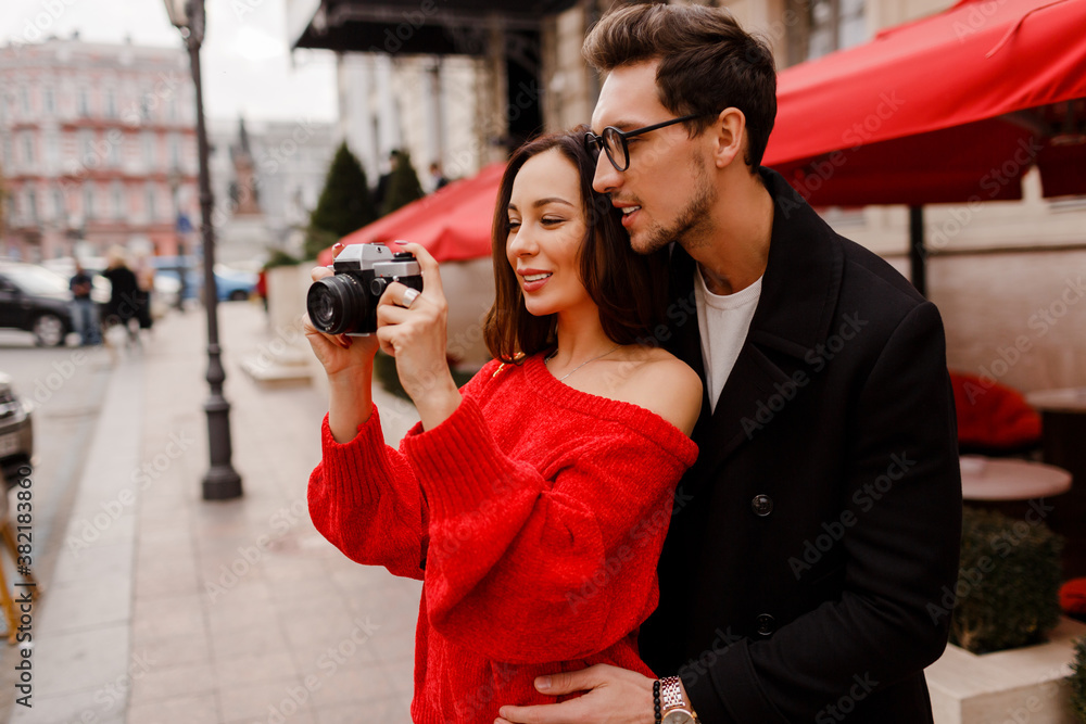 Traveling couple embarrassing and  posing on the street on holiday. Romantic mood.  Lovely brunette woman holding film camera. Valentine’s Day.