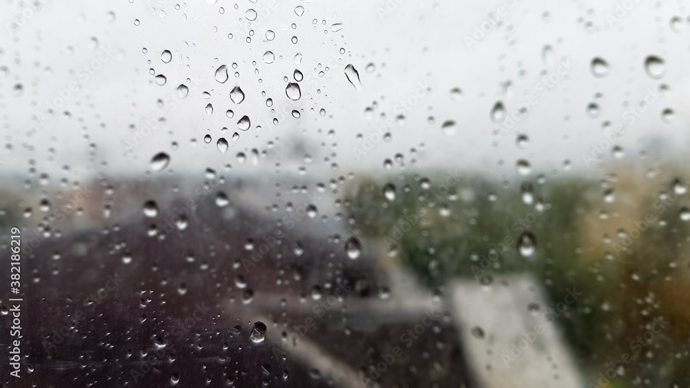 Wet window with drops on the background of the autumn city in cloudy weather. View from the window in the rain. Water drop on glass window during rain with blurred background of city scene Wet window with drops on the background of the autumn city in cloudy weather. View from the window in the rain. Water drop on glass window during rain with blurred background of city scene