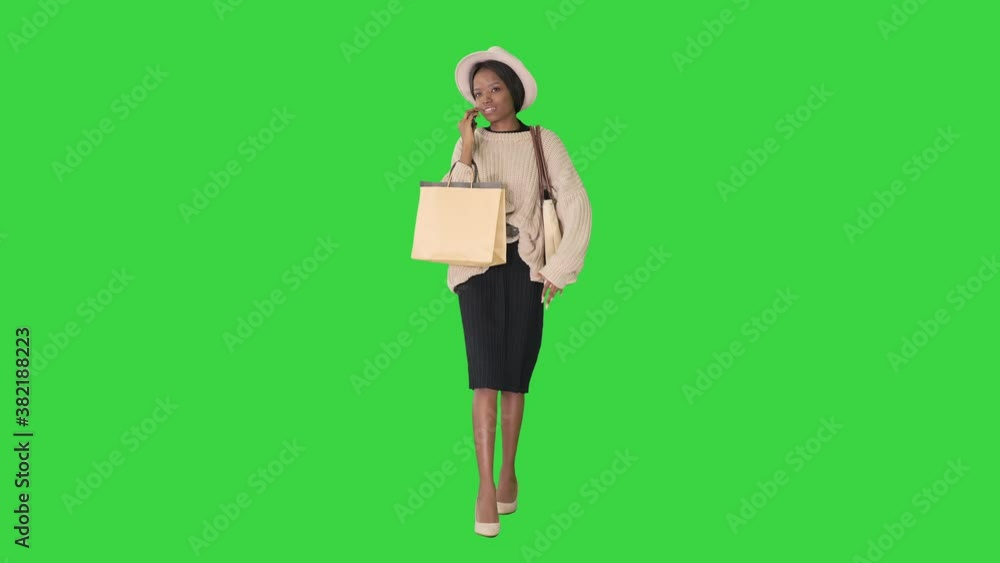 African american girl in oversized knitwear and hat talking on her phone while walking with shopping bags on a Green Screen, Chroma Key. African american girl in oversized knitwear and hat talking on her phone while walking with shopping bags on a Green Screen, Chroma Key.