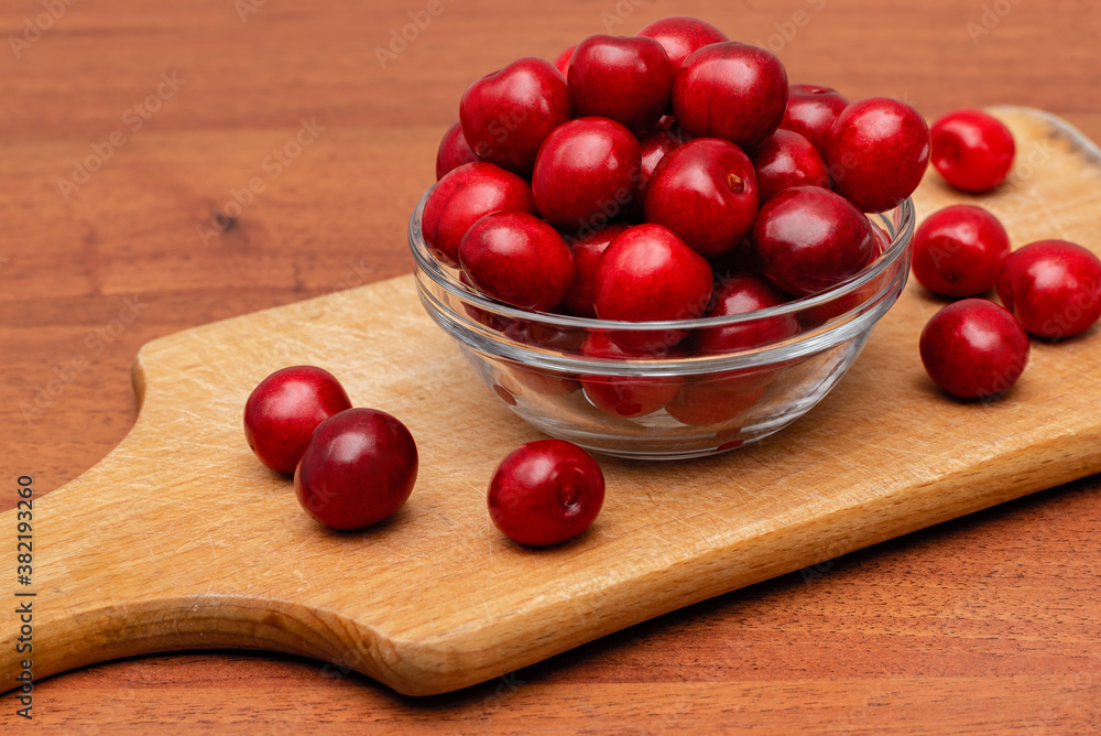 fresh black cherries in glass plate on wooden board on a wooden background