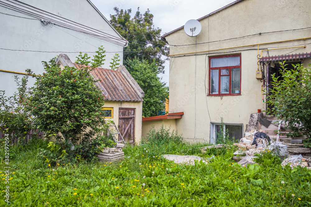 Obraz premium Overgrown yard near the old house. Old well-kept one-storey house and a yard overgrown with grass and flowers