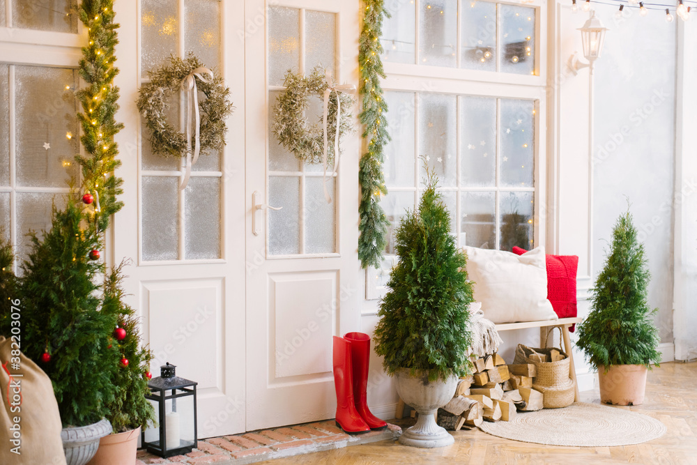 The white private house is decorated with small Christmas trees and lanterns, a bag of gifts. A bench with pillows near the front door of the house and wood under it