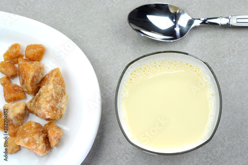 Hot jaggery milk in a glass cup with jaggery chunks in a plate photo