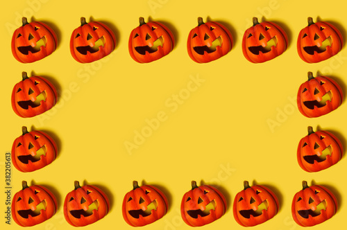 Pattern. On a yellow background, there are many pumpkins with a carved smile. Pumpkins standing in a glad around the perimeter. Free space in the center. Halloween celebration concept.