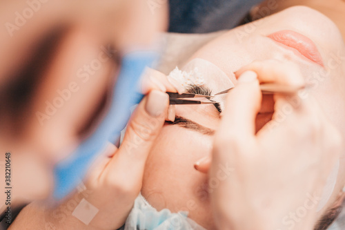 Gluing a bunch of artificial eyelashes on a girl eyelid - eyelash extension procedure woman
