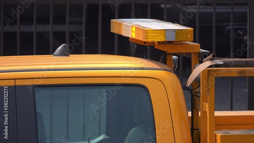 Yellow lights flash on a truck's light bar up close on a city street during the day.