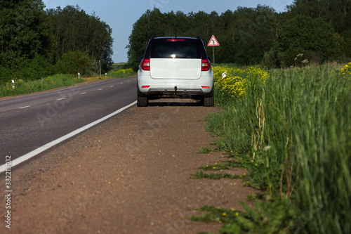 A modern white car sits at the edge of the road next to a green field while traveling and looking for new routes. Outdoor weekends, local travel and summer trips