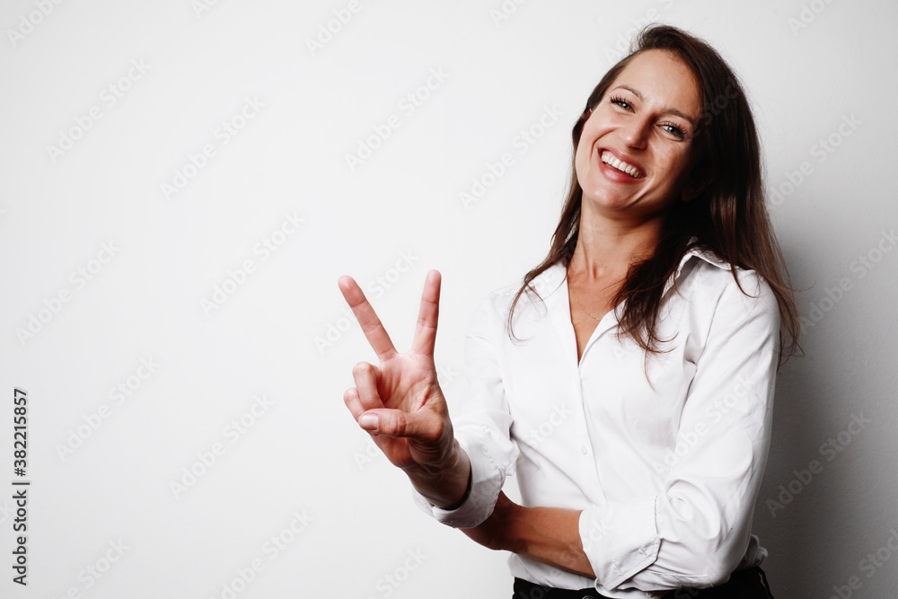 Portrait of young woman showing Victory gesture with fingers, posing against white background. Space for text. Portrait of young woman showing Victory gesture with fingers, posing against white background. Space for text.