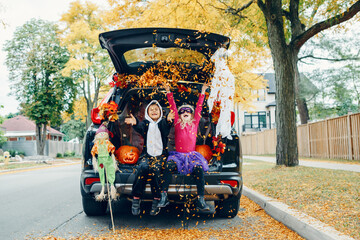 Trick or trunk. Children celebrating Halloween in trunk of car. Boy and girl with red pumpkins celebrating traditional October holiday outdoors. Social distance during coronavirus covid-19.