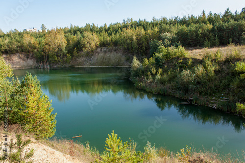 Suburbs of Grodno. Belarus. Green lake. Forest on the shore and its reflection in the water. The sun s rays on the crowns of trees and on the surface of the water.