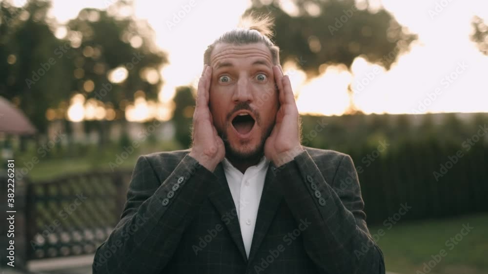 Portrait of bearded handsome amazed brunette guy with raised hands at sunset background. Shocked Businessman. Young Man Surprised. Portrait of bearded handsome amazed brunette guy with raised hands at sunset background. Shocked Businessman. Young Man Surprised.
