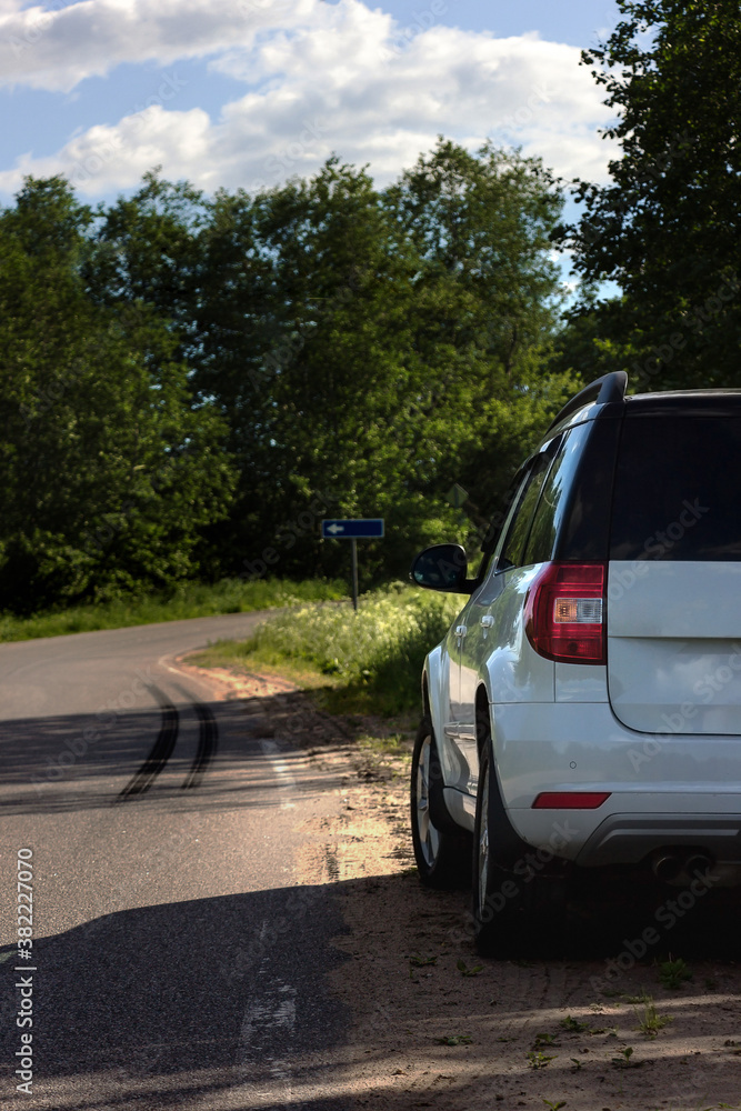 A modern white car sits at the edge of the road next to a green field while traveling and looking for new routes. Outdoor weekends, local travel and summer trips