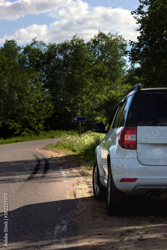 A modern white car sits at the edge of the road next to a green field while traveling and looking for new routes. Outdoor weekends, local travel and summer trips © HAMERCAT