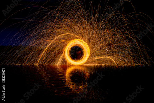 Burning Steel Wool spinning, Trajectories of burning sparks on the surface of water lake at the background of spring night landscape