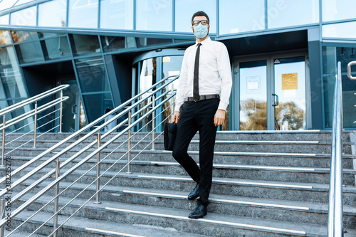 young businessman in business clothes, a man in a medical protective mask on his face, leaves the office building after a working day, Quarantine, coronavirus © Shopping King Louie