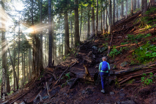 Girl Outdoor Hiking on a Trail in the Woods with Sunny Sunrays coming between the trees. Taken in Cypress Provincial Park, West Vancouver, British Columbia, Canada.