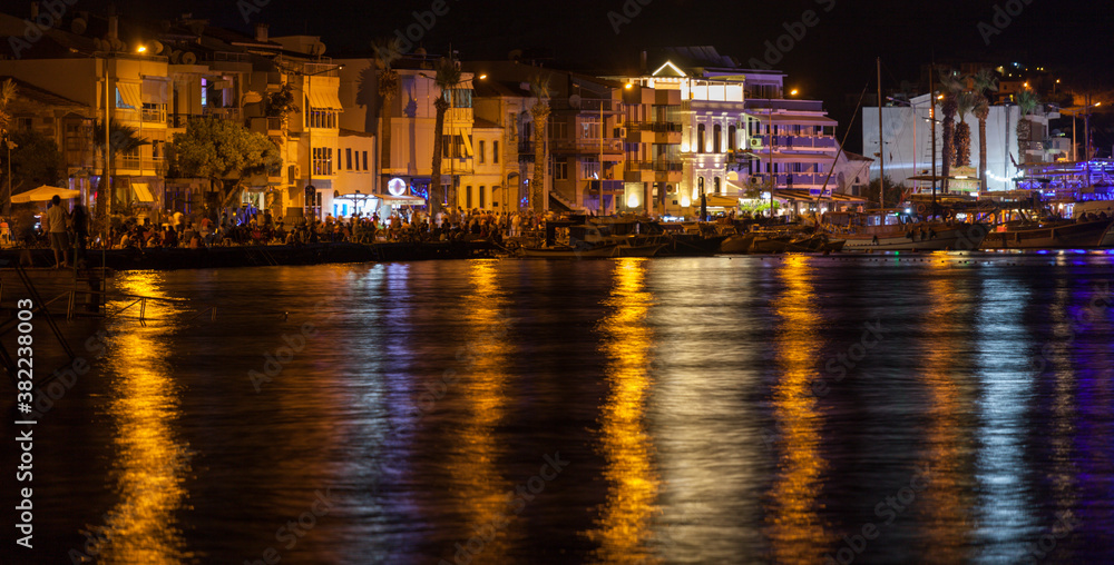 The night view of Eski Foca (in EN: old Phokaia) with nice light reflections over the sea. Highly crowded seaside and everyone is walking around.