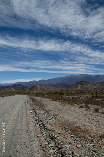 Desert route across the death valley. View of the dirt road  desert and mountains under a beautiful blue sky with clouds.