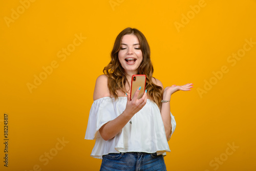 Excited woman with digital device. Studio shot of shocked girl holding smartphone, emotional