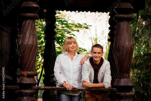 A beautiful woman,blonde,middle-aged,in a white shirt and jeans,with a large son,stands near an eco-friendly wooden house photo