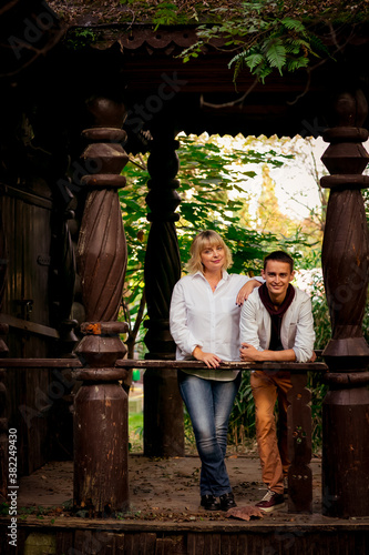 A beautiful woman,blonde,middle-aged,in a white shirt and jeans,with a large son,stands near an eco-friendly wooden house photo