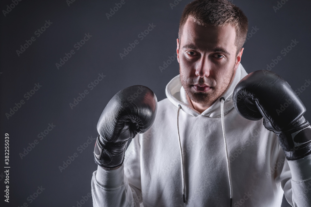 Young man in boxing gloves and a white sweatshirt on a dark background in the studio. The concept of victories and battles Young man in boxing gloves and a white sweatshirt on a dark background in the studio. The concept of victories and battles