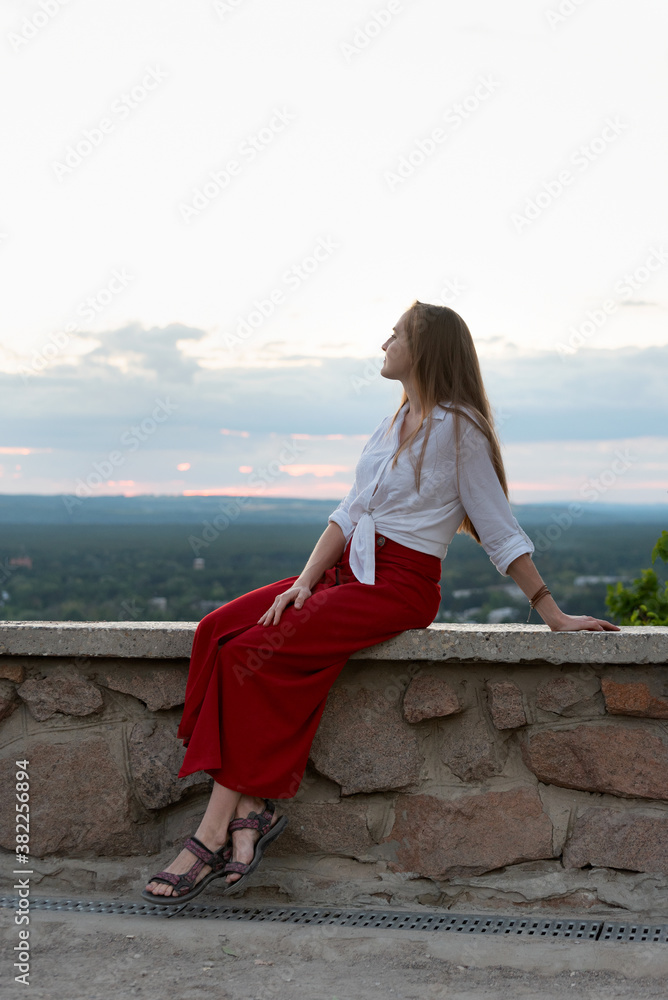 Beautiful young woman on hill is resting with view of nature. Vertical frame
