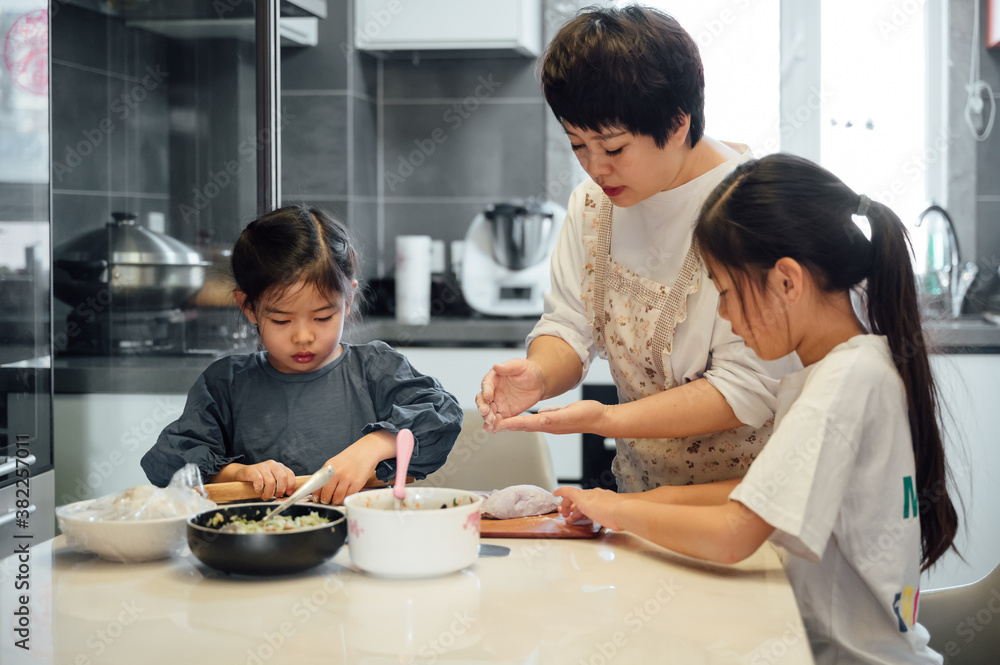 Chinese mother and her two daughters making dumplings together at home