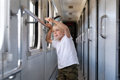 Fair-haired boy stands in railway carriage and looks out window. Rail travel
